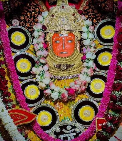 Jeen Mata’s face in pushp shringar, framed by pink and white rose garlands and golden ornaments