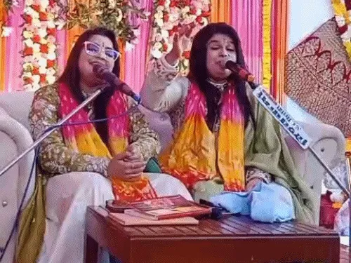 Two singers leading devotional songs at a bhajan sandhya, seated before microphones beneath flower decorations