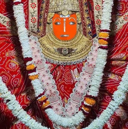 Close darshan of Jeen Mata’s face with golden crown and necklace, adorned with a red bandhani chunari and white garlands